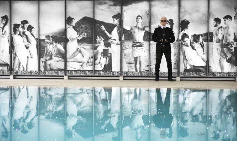O Καρλ Λάγκερφελντ φωτογραφημένος στην εσωτερική πισίνα του Le Metropole στο Μόντε Κάρλο με τις σκηνές από την ελληνική μυθολογία να κοσμούν τον περίγυρο